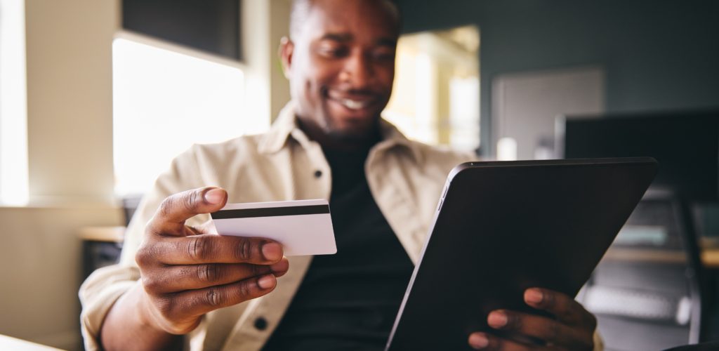 Smiling Man making online payment on tablet computer focused on credit card